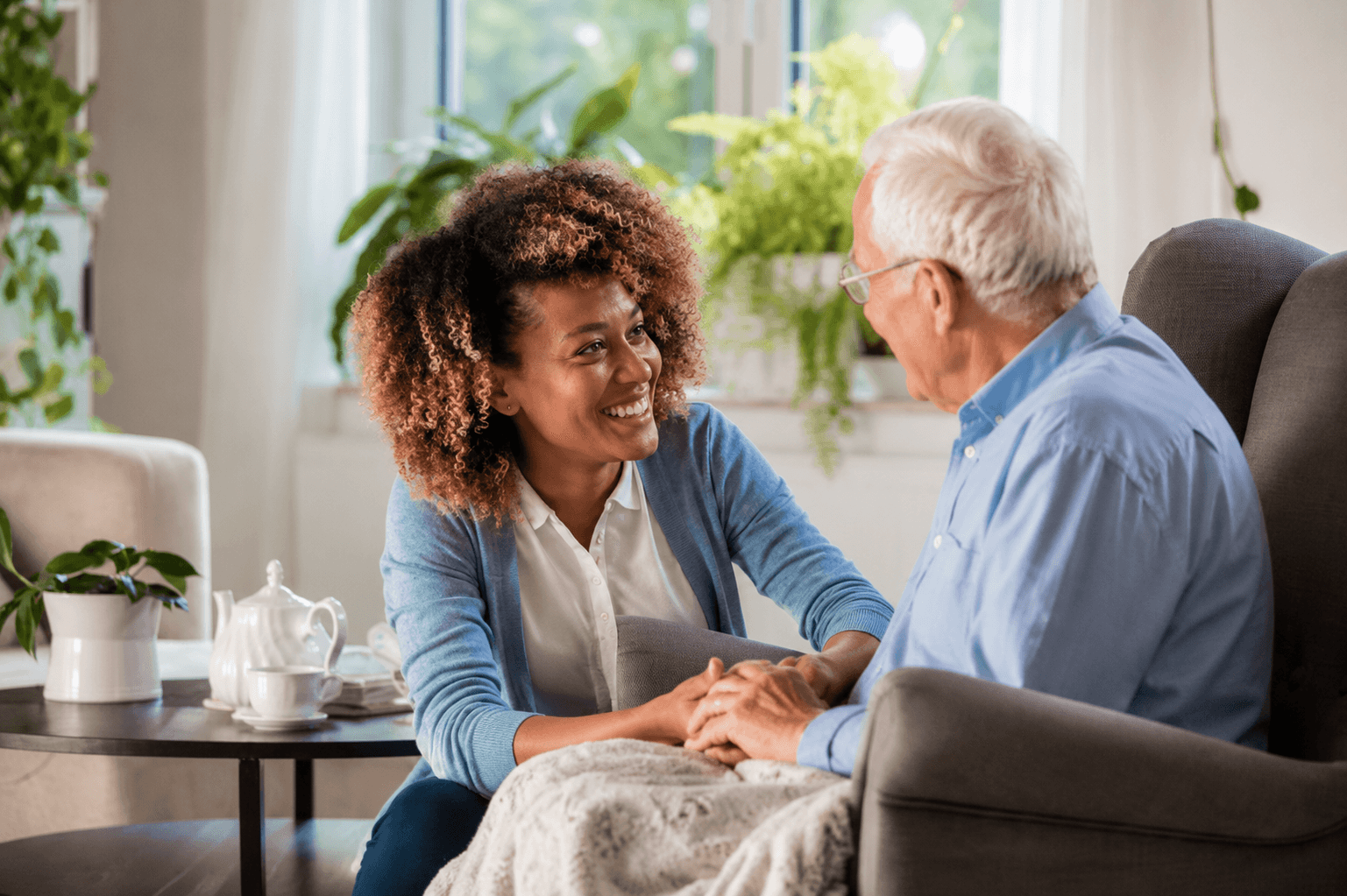 Female companion listening attentively and holding an older man’s hands at home