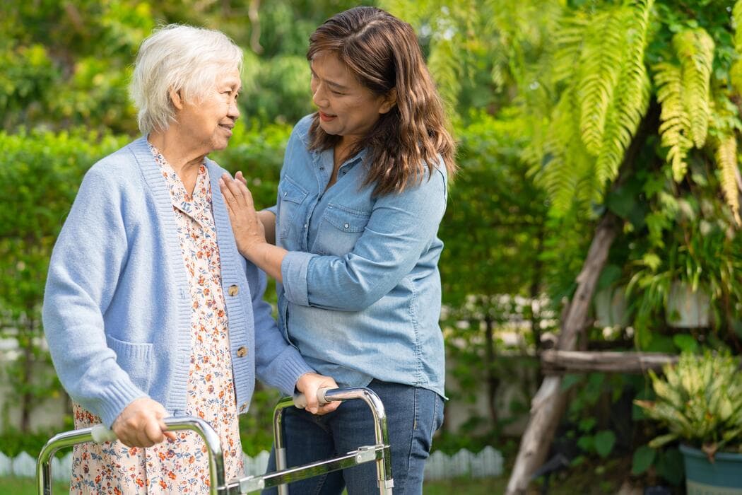 Companion supporting an older woman using a walker in a garden