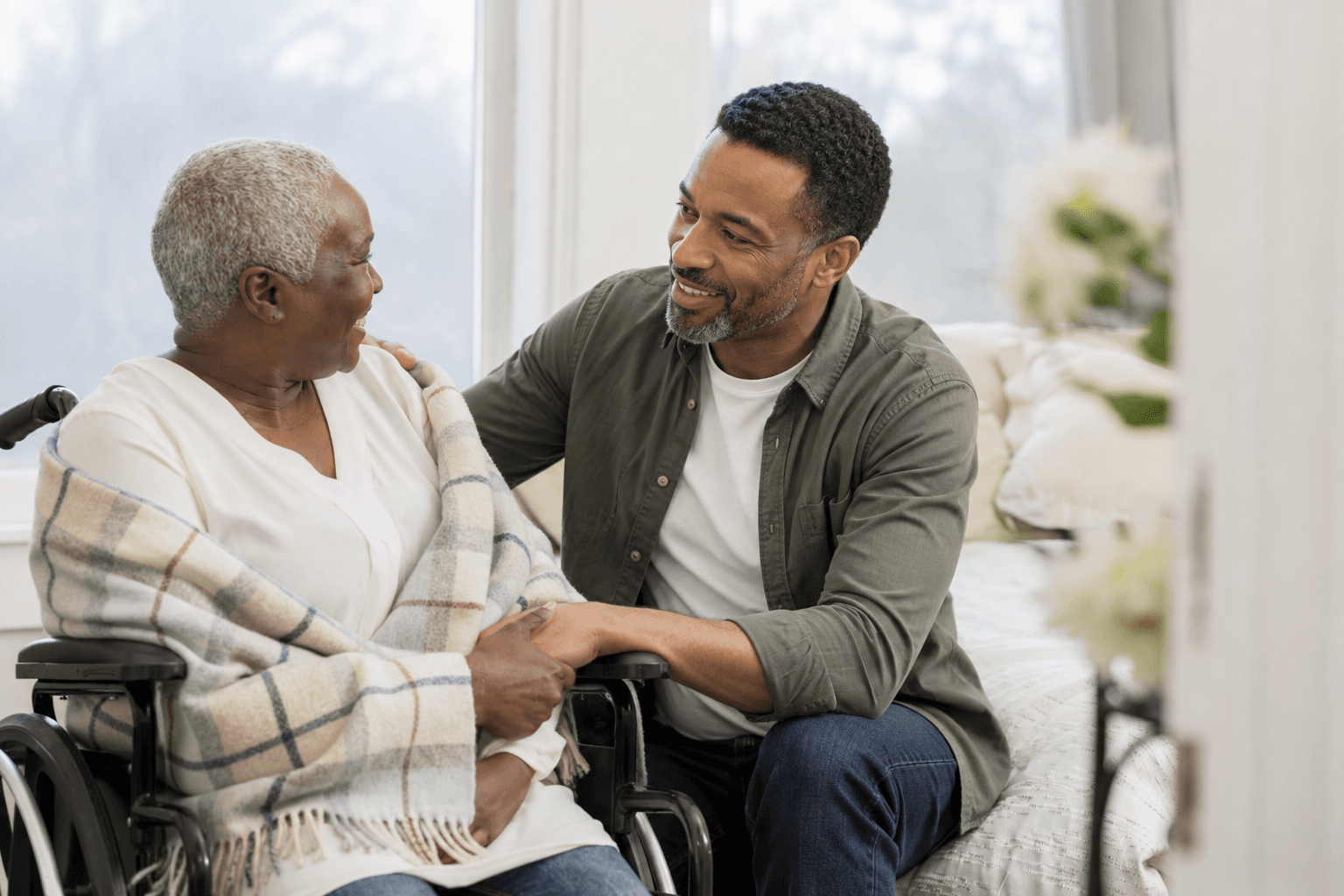 Male companion offering calm reassurance to an older woman seated in a wheelchair